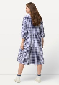 Blau-weiß kariertes Kleid mit Dreiviertelärmeln, einem gestuften Design und einem mittellangen Saum, kombiniert mit weißen Knöchelstiefeln.