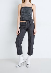 Top corto in denim grigio con spalline sottili, abbinato a pantaloni grigi a righe con dettagli in bottone e scarpe col tacco argentate.