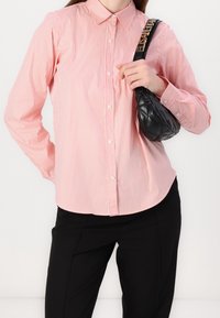 Langsleeve overhemd met rode en witte strepen en een puntige kraag, gecombineerd met een zwarte gewatteerde handtas en zwarte broeken.