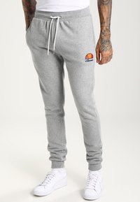 Pantalones de chándal grises con cintura elástica y cordón, que presentan un pequeño logotipo colorido en el muslo izquierdo. Material de algodón suave.