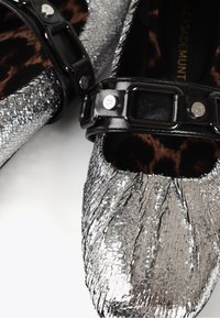 Metaliczne srebrne płaskie buty z pomarszczoną teksturą, czarny pasek z elementami w kolorze srebrnym oraz detal na wkładce w panterkę.