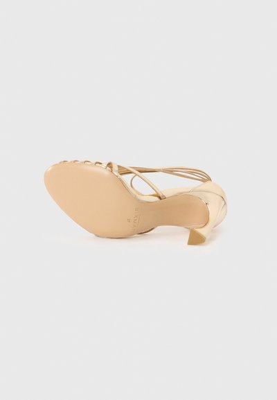 Beige heeled sandal with a pointed toe and thin straps. Features a glossy finish and a short, triangular heel. Smooth sole.