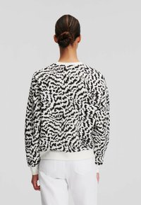 Musta-valkoinen kuvioitu svetari, jossa pitkät hihat, resorinen pääntie ja hihansuut. Kankaassa on sileä pinta ja abstrakti kuvio.