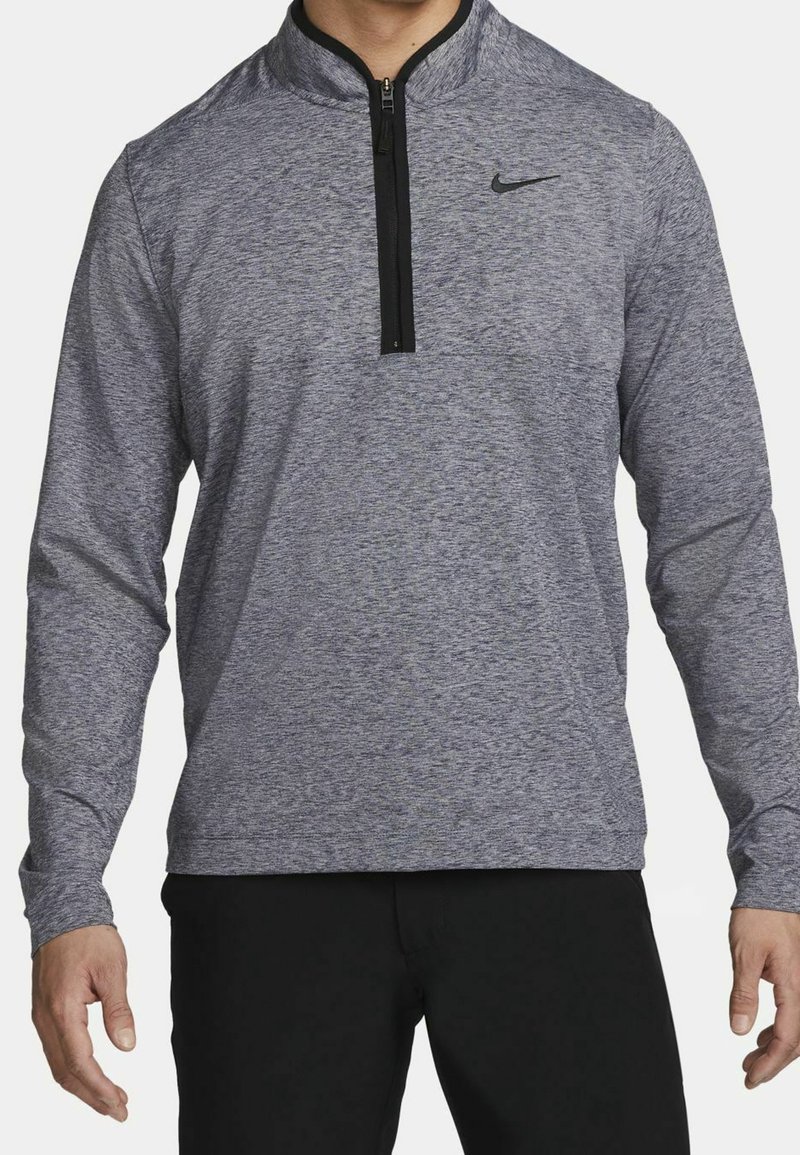 Polo gris à manches longues en tissu texturé, avec fermeture éclair noire et col. Logo Nike sur la poitrine gauche.