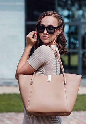 Beige kožená taška přes rameno s dvěma popruhy, ozdobená stříbrnými prvky a minimalistickým designem. Hladký povrch, prostorný tvar.