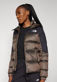 Brązowa i czarna kurtka puchowa z zamkiem z przodu, kapturem i bocznymi kieszeniami. Wykonana z teksturowanego, lekkiego, izolowanego materiału.