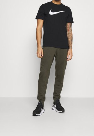 Sort Nike t-shirt med hvidt logo, olivengrønne joggingbukser og sorte Nike sneakers med hvide detaljer. Afslappet atletisk outfit.