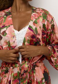 Blommönstrad kimono i rosa, grön och röd, med midjeband och lösa ärmar. Lager på en vit spetsblus.