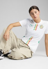 White athletic shirt with green, red, and yellow pattern along the chest. Features a round neck and short sleeves. Black Puma logo on shoulder.