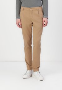 Tan cotton pants with a straight fit, featuring a front zipper and button closure, side pockets, and a smooth texture. Paired with white sneakers.