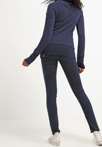 Felpa blu marina con retro a fantasia, maniche lunghe e aperture per il pollice, abbinata a jeans skinny scuri e calzature bianche.