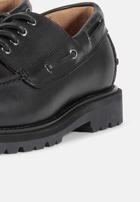 Sorte lærersko med lav profil, rund tå og solid gummisåle med et mønster av lugger. Metallhull og lisser. 