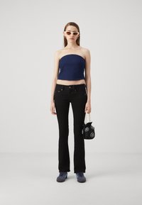 Top sin tirantes azul marino, pantalones vaqueros negros acampanados, zapatillas azules y un bolso negro con patrones florales y un asa de perlas. Fondo claro.