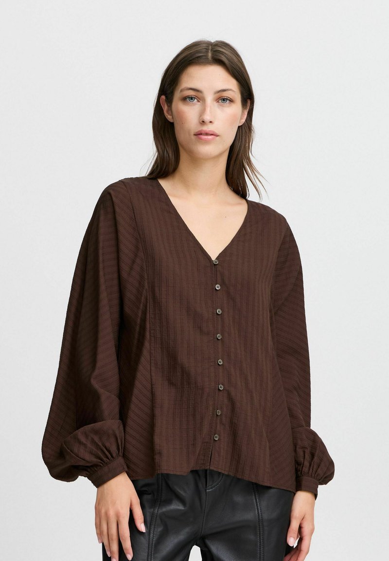Brun, texturerad blus med V-hals, puffärmar och framknäppning. Har subtila vertikala ränder och en lös passform.