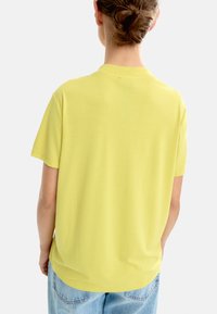 Żółta krótki rękaw T-shirt wykonana z miękkiego materiału, z okrągłym dekoltem i luźnym krojem. Projekt charakteryzuje się gładką fakturą i minimalnymi detalami.