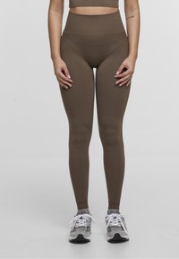 High-waisted brown leggings made of stretchy fabric, featuring seamless design and a smooth texture, paired with grey athletic shoes.