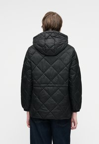 Veste matelassée noire avec capuche, présentant des motifs en losange et des poignets élastiques. Le matériau semble brillant et rembourré, offrant une isolation.