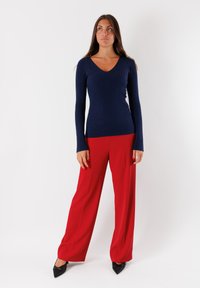 Maglietta a maniche lunghe blu navy con scollo a V, abbinata a pantaloni rossi a gamba larga, completata da décolleté nere appuntite. Design semplice e aderente.