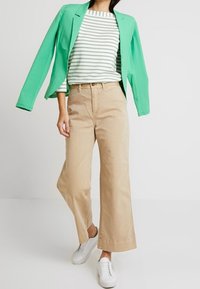 Blazer vert menthe, haut rayé blanc et vert, pantalon large beige et baskets blanches. Tissus texturés et design décontracté.