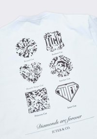 T-shirt bianca con stampe grafiche di tagli di diamante: Rotondo, Radiante, a Cuore, Asscher, Principessa e Iuter Cut, con testo sottostante.