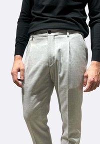 Pantaloni su misura grigio chiaro con pieghe frontali, taglio ampio e texture liscia. Presentano una chiusura con bottoni e tasche laterali.