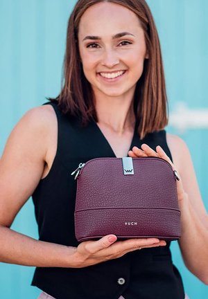 Burgundská kožená kosmetická taška s texturovaným povrchem, stříbrnými doplňky a logem značky, se zaobleným tvarem a dvojitými zipy.