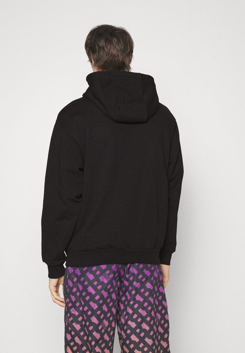 Felpa nera con cappuccio, dal fit rilassato, con polsini e orlo a costine, abbinata a pantaloni corti colorati con motivo in gradiente viola e rosa.