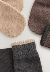 Calze lavorate a maglia in beige e marrone scuro, caratterizzate da trame a coste e a spina di pesce. Le punte hanno accenti a contrasto di colore crema.