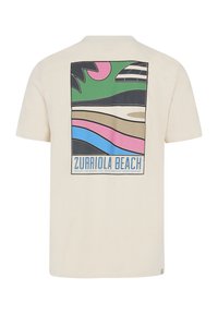 Beige t-shirt med et farverigt grafiktryk på ryggen, der viser bølger, palmeblade og teksten "Zurriola Beach" i blå. Kortærmet, afslappet pasform.