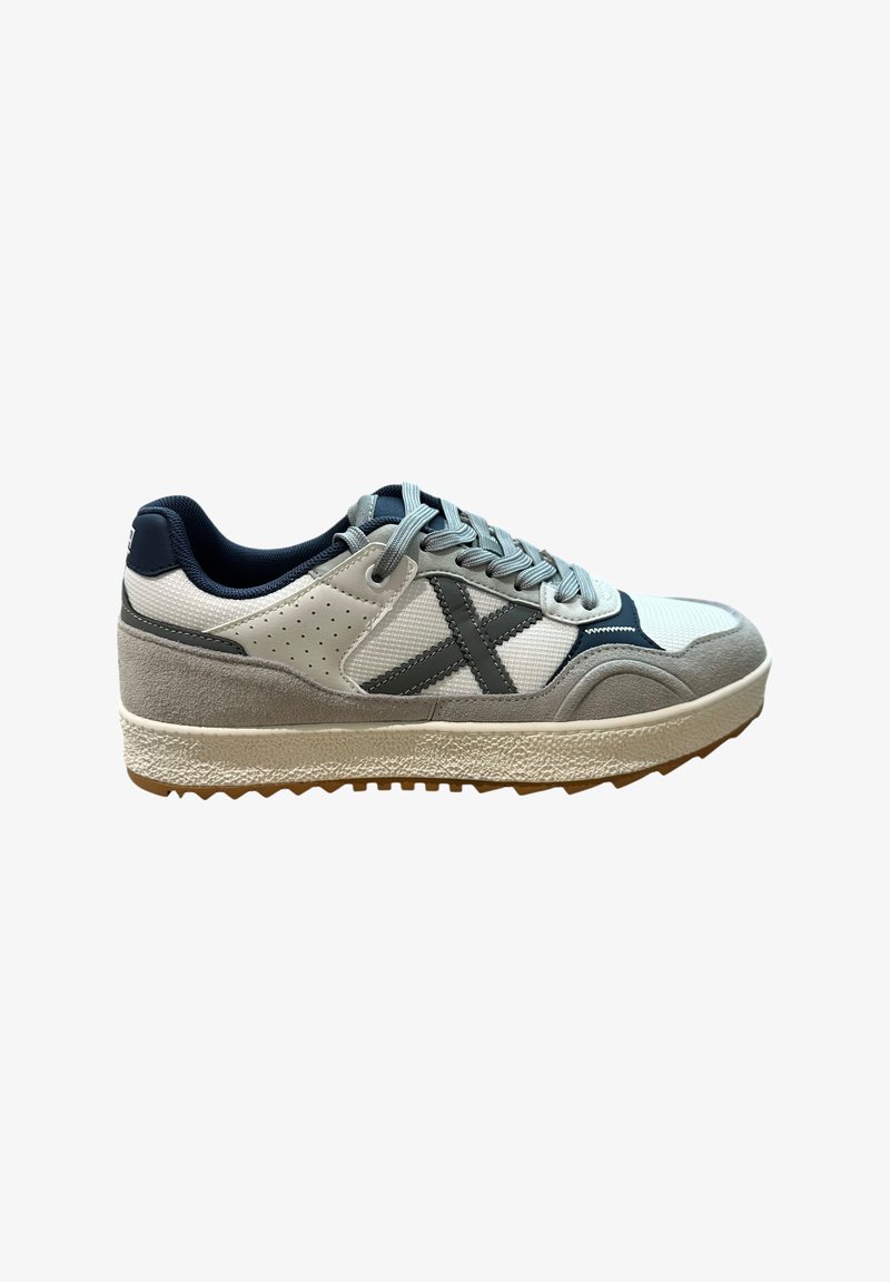 Zapatilla blanca y gris con suela texturizada, acentos en marino y detalles perforados. Presenta un diseño de cordones que proporciona soporte.