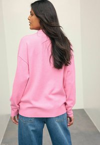 Übergröße pinker Sweatshirt mit gerippten Bündchen und Saum, kombiniert mit hellblauen Jeans. Der Stoff wirkt weich mit einer glatten Textur.