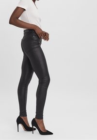 Zwarte neplederen skinny broeken met een gladde textuur en subtiele glans, gecombineerd met elegante zwarte hoge hakken en een getailleerde witte top.