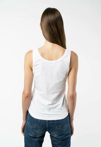 Weißes Baumwoll-Tanktop ohne Ärmel mit rundem Ausschnitt und glatter Textur, kombiniert mit blauen Jeans.