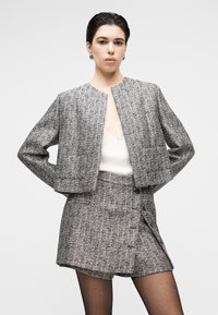 Chaqueta de tweed gris con un diseño corto, combinada con una falda a juego. La textura es estructurada, con cierre de botones y detalles delicados.