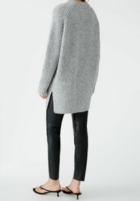 Pull en tricot gris clair avec une coupe décontractée et une texture côtelée, assorti à un pantalon en cuir noir ajusté et des sandales à talons noirs simples.