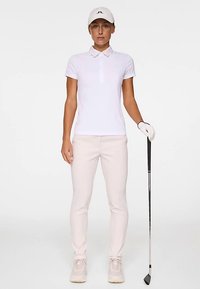 Biała koszulka polo z kołnierzykiem, jasnoróżowe dopasowane spodnie, biała czapka, biała rękawica golfowa i kij golfowy. Gładka tkanina, swobodny krój.