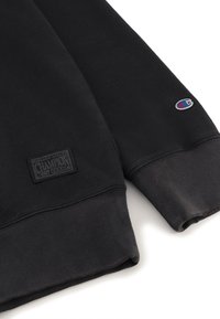 Sudadera negra de mezcla de algodón, con puños y dobladillo acanalados, una etiqueta tejida en la parte frontal y un pequeño parche con el logo en la manga.