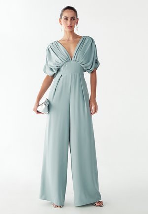 Bledomodrý overal s hlbokým výstrihom do V a nadýchanými rukávmi. Má priliehavý korzet a široké nohavice, vyrobený z hladkej látky.