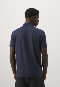 Navy polo shirt in lightweight, smooth fabric with a collar and short sleeves. Subtle logo detail on the sleeve, back view, and minimal design.