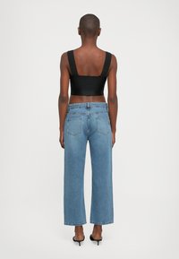 Black sleeveless top with wide straps, paired with light blue wide-leg jeans. The jeans have a classic five-pocket design and cuffed hems.