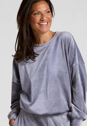 Velvet pullover in zachte lavendel, met een relaxte pasvorm, verlaagde schouders en brede geribbelde halslijn. Soepele textuur, casual ontwerp.
