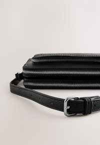 Črna usnjena torba z več žepki na zadrgo, ravna pravokotna oblika, nastavljiv trak in srebrna zaponka kot okras.