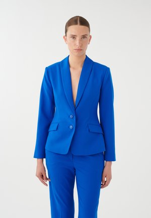 Blazer blu su misura con rever a buco, due bottoni e tasche frontali, abbinato a pantaloni coordinati, texture liscia, design aderente.