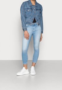 Ljusblå jeansjacka med en kortad passform, två bröstfickor och silverdetaljer, matchad med ljusblå skinny jeans och vita sneakers.