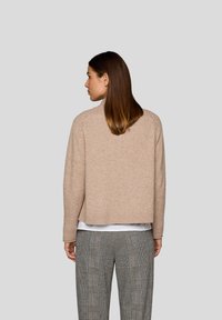 Beiger Strickpullover mit Rundhalsausschnitt, kurzem Saum und feiner Struktur, kombiniert mit karierten, hoch taillierten Hosen.