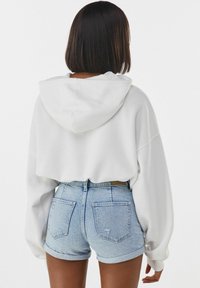 Vit kortärmad hoodie med dragsko i huvan, parat med ljusblå denimshorts med uppvikta fållar och bakfickor.