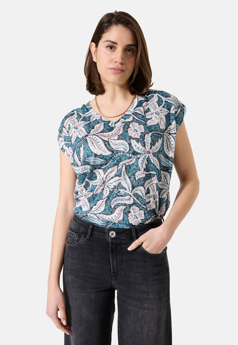 Bloemenpatroon top in teal en wit, met cap sleeves en een relaxed fit. Gepaard met zwarte denim jeans.