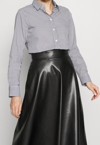 Raidoitettu nappikauluspaita vaaleansinisessä ja valkoisessa, yhdistettynä korkeavyötäröiseen mustaan nahkahameeseen, jossa on sileä tekstuuri ja tyylikäs siluetti.