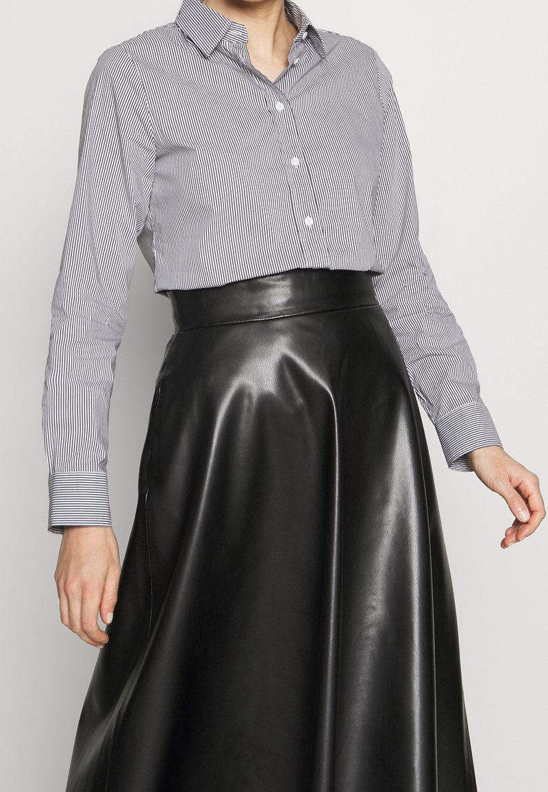 Raidoitettu nappikauluspaita vaaleansinisessä ja valkoisessa, yhdistettynä korkeavyötäröiseen mustaan nahkahameeseen, jossa on sileä tekstuuri ja tyylikäs siluetti.