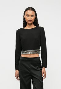 Μαύρη κοντή μπλούζα με μακριά μανίκια που διαθέτει ασημένια αλυσίδα στη μέση. Το ύφασμα είναι λείο με καλοσχηματισμένη εφαρμογή και στρογγυλή λαιμόκοψη.